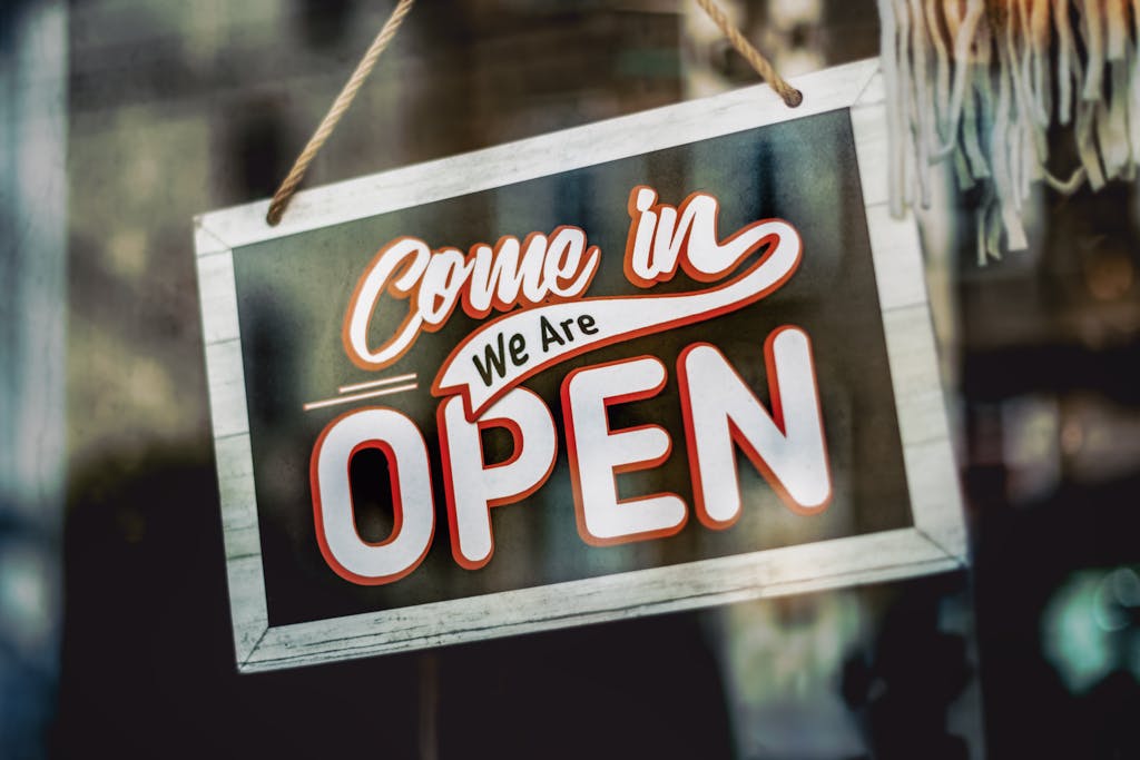 A welcoming'Come in, We Are Open' sign hanging on a glass window of an urban shop.